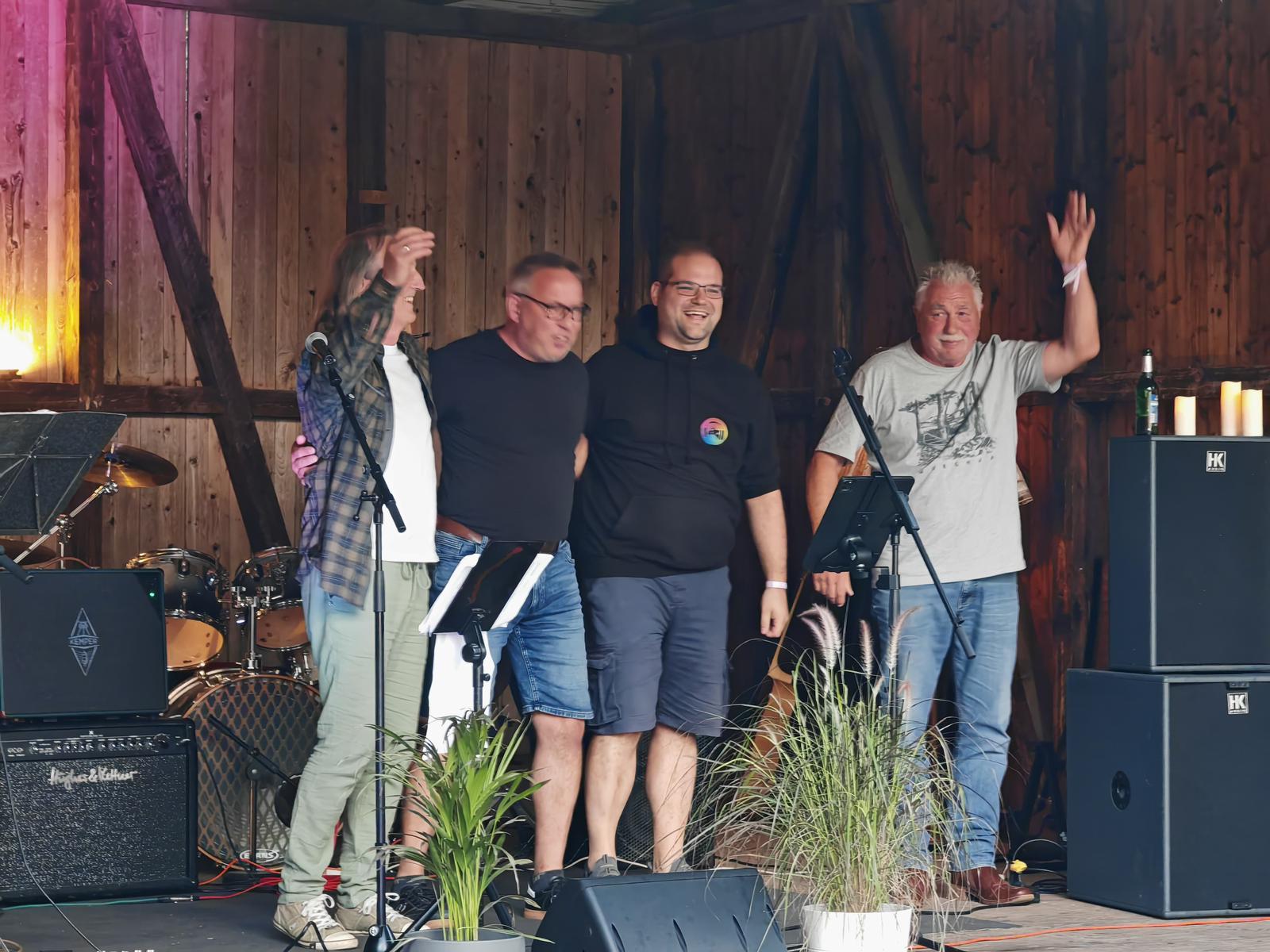 Eine hölzerne Open-Air Bühne. Andreas, Voker, Carsten und Rüdiger verabschieden sich vom Publikum