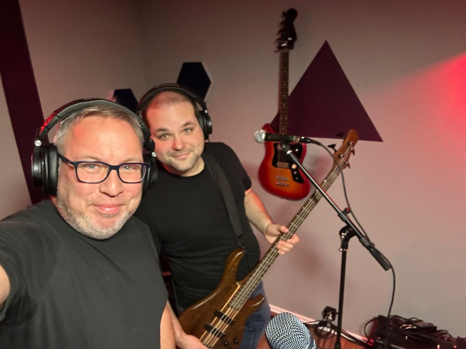Volker und Carsten machen Aufnahmen im Studio. Carsten hat einen Bass in der Hand, an der Wand dahinter hängt ebenfalls eine Bassgitarre.